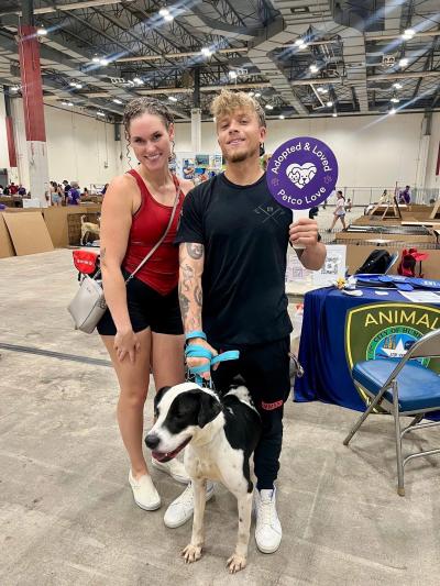 Diesel the dog with his adopters, one of whom is holding an "Adopted & Love Petco Love" sign 